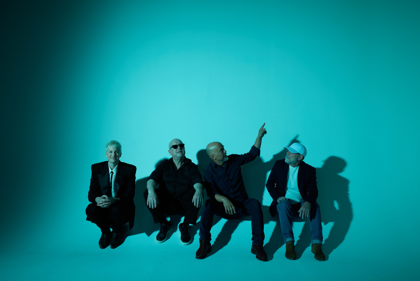Members of the band the pixies sitting on the floor of a studio with blue lighting 